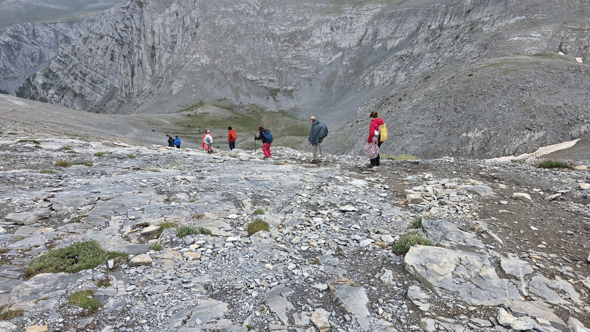 Hikers descending a rocky mountainside beneath the steep ridges of Mount Olympus.